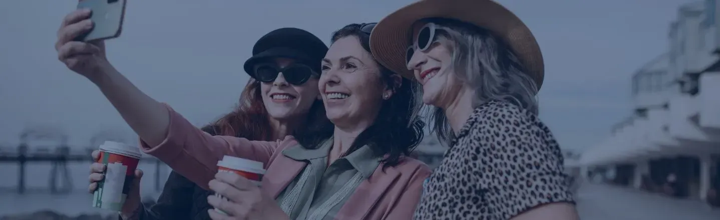 Three friends taking a selfie outdoors, smiling and holding drinks.