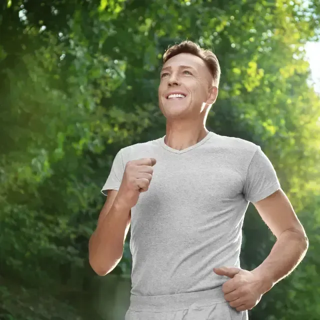 Smiling person in a gray T-shirt jogging in a sunlit green park