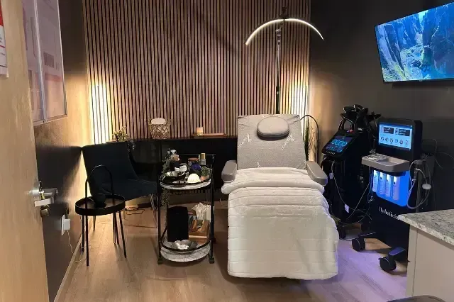 Modern treatment room with reclining spa chair, wall decor, small table, and medical equipment at right