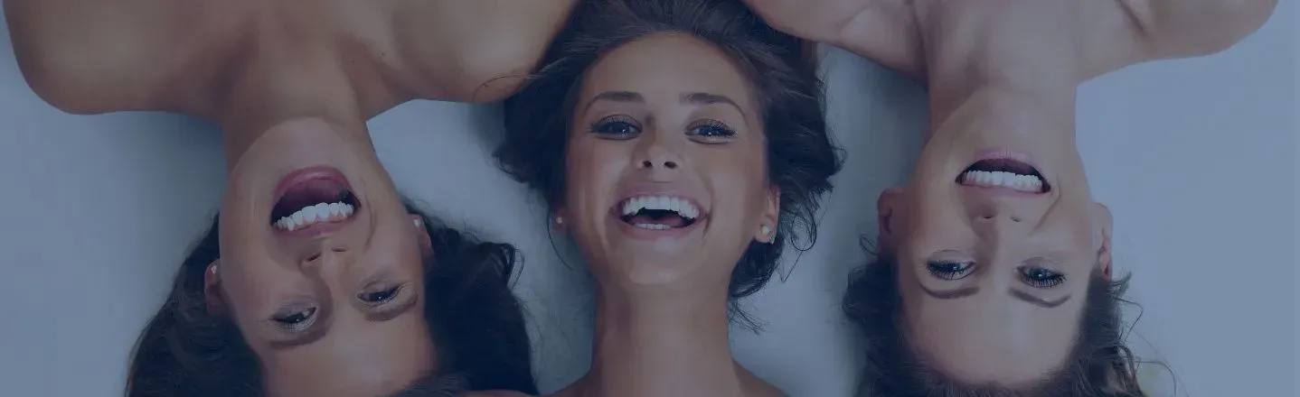 Three smiling women lying head-to-head, faces upside down against a blue background