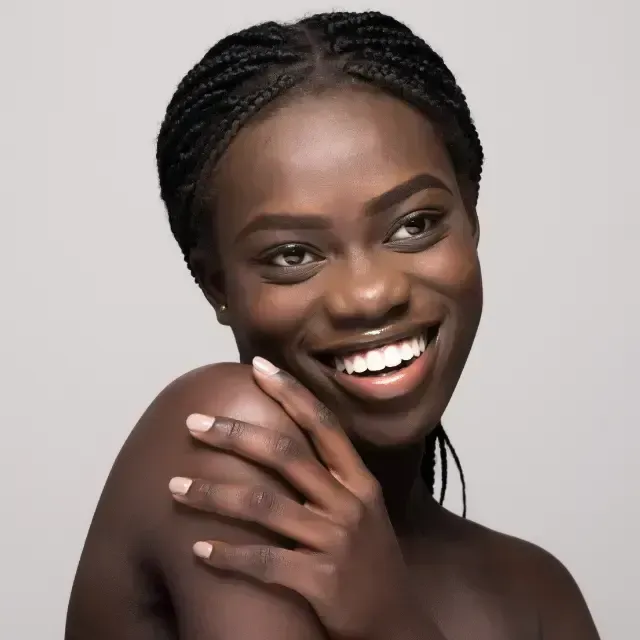 Smiling person with braided hair, resting hand on shoulder against a light gray background