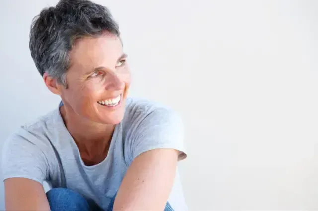 Smiling person in a light gray shirt sitting against a white background