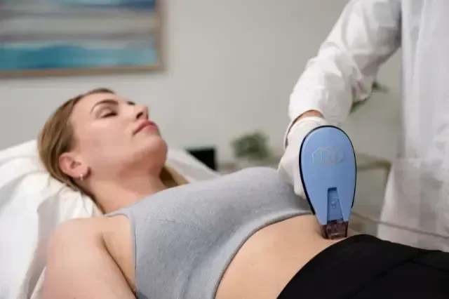 Clinician using a handheld ultrasound device on a patient's abdomen in a medical exam room