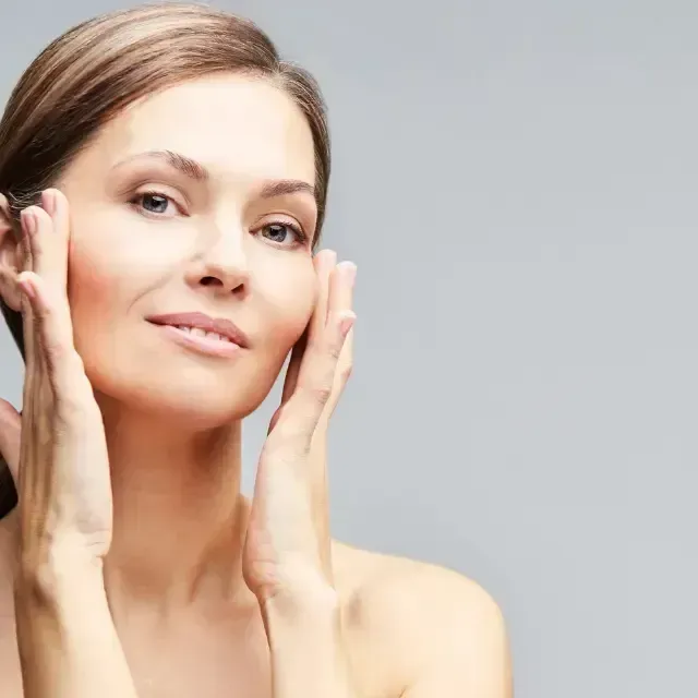 Woman gently touching her face against a light gray background