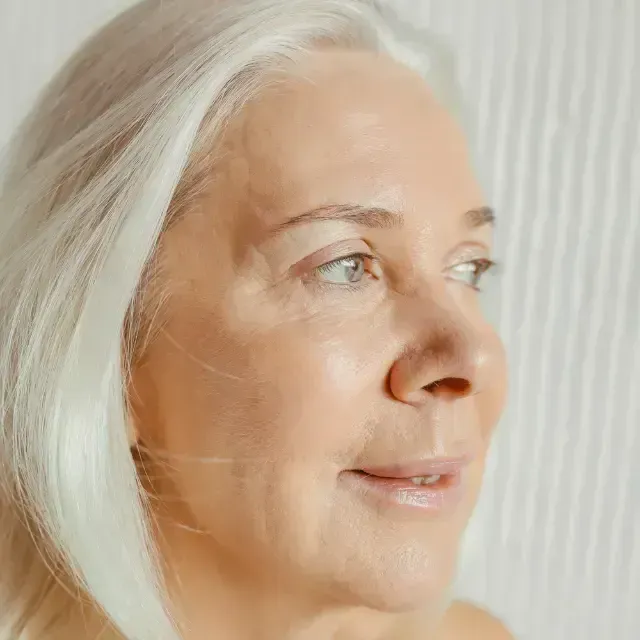 Close-up profile of a smiling woman with white hair against a soft, light background