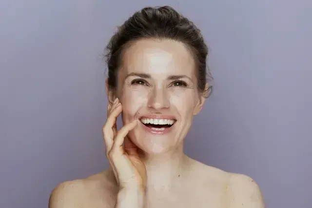 Smiling woman touching her face against a plain gray background
