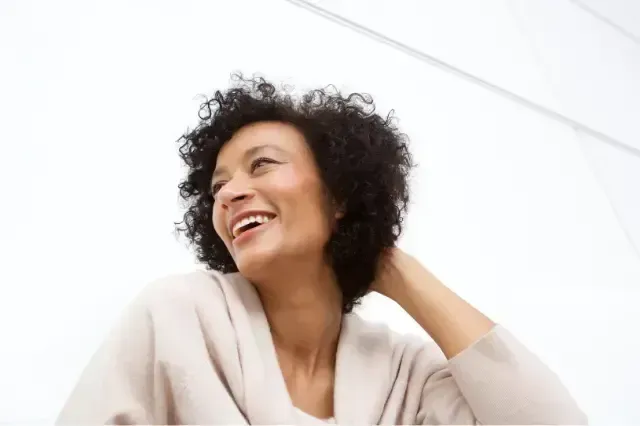 Smiling woman with curly hair, wearing a light sweater and looking off to the side against a white background