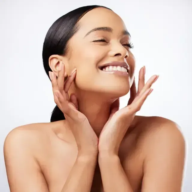 Smiling woman touching her face with both hands against a white background