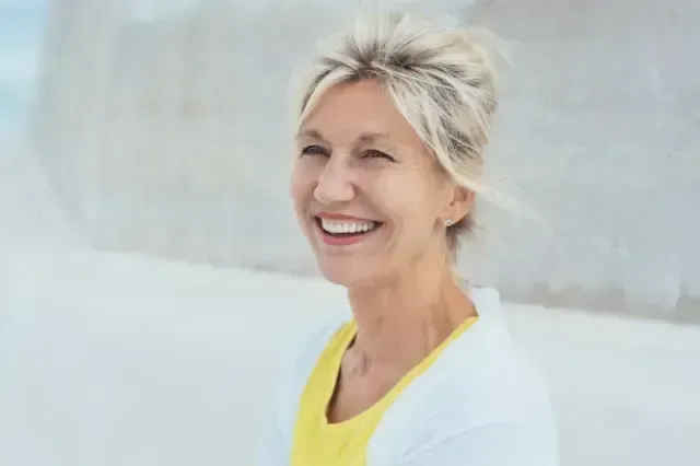 Smiling woman with short blond hair in a yellow top against a soft light gray background