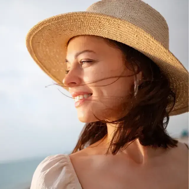 Woman in a straw hat smiling in profile by the sea on a sunny day