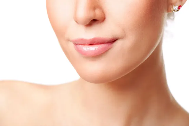 Close-up of a woman’s lower face and neck with soft pink lips and a small earring against a white background