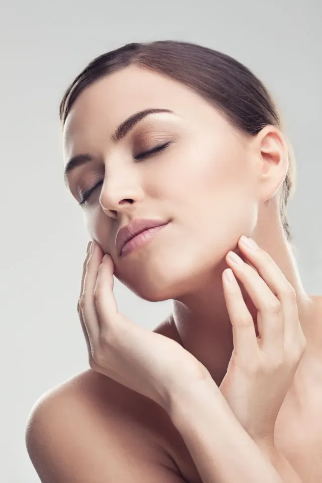 Woman with closed eyes touching her face against a soft gray background