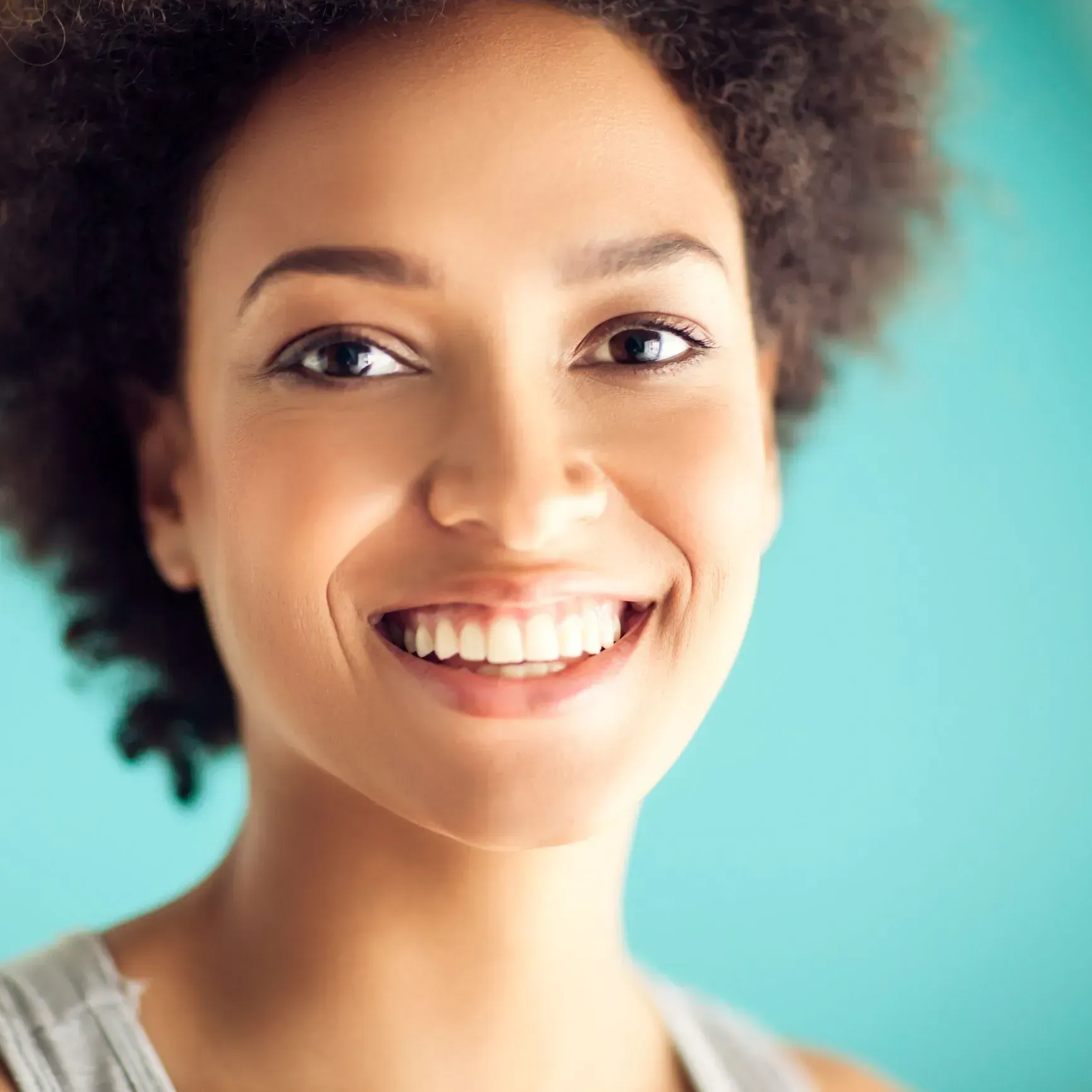 Smiling person with curly hair against a turquoise background