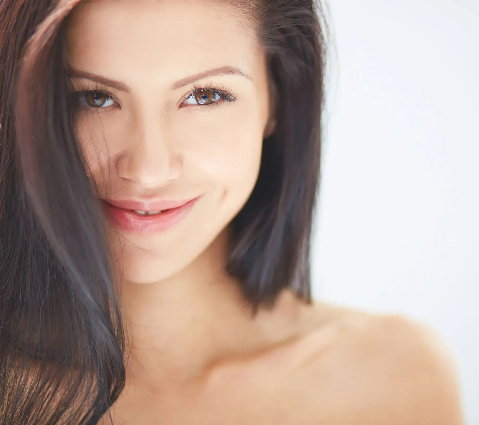 Close-up portrait of a smiling woman with dark hair against a bright white background
