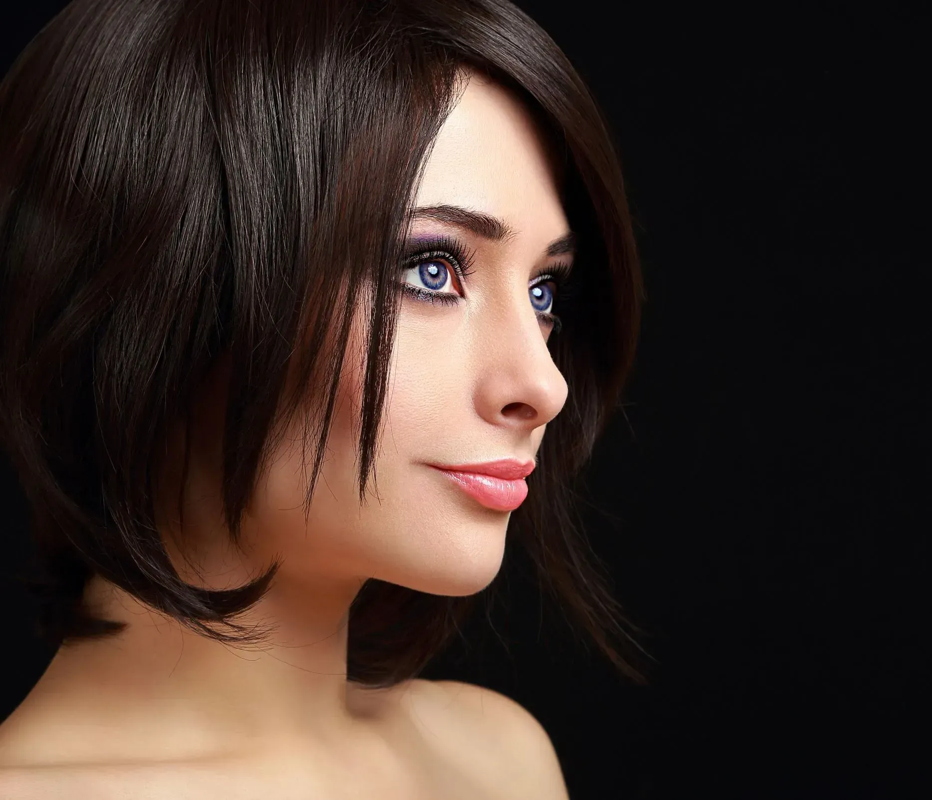 Close-up portrait of a person with short dark hair, blue eyes, and a slight smile against a dark background