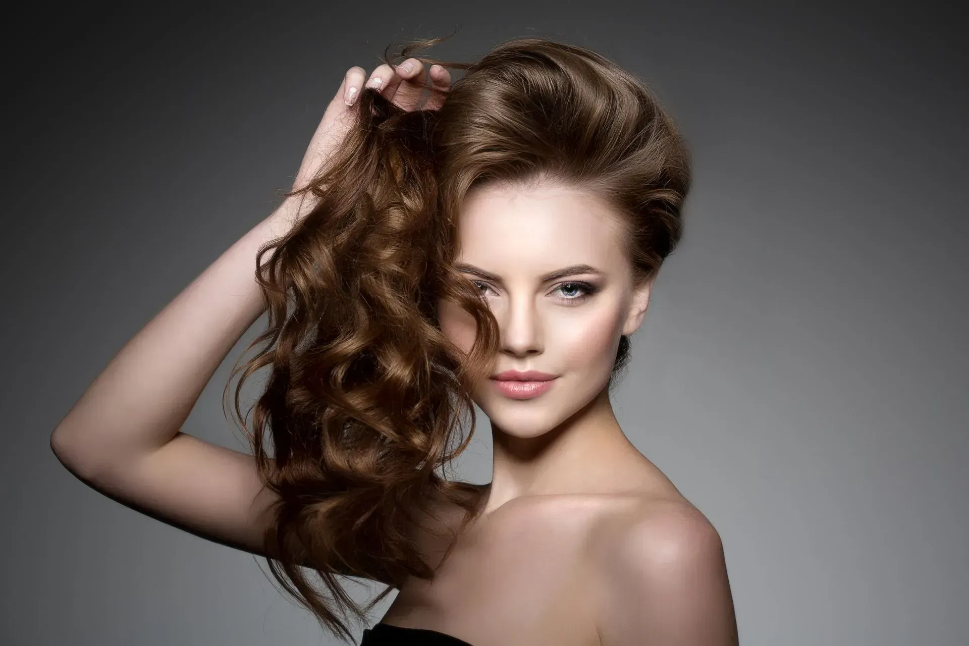 Woman with voluminous curly brown hair posing against a gray studio background