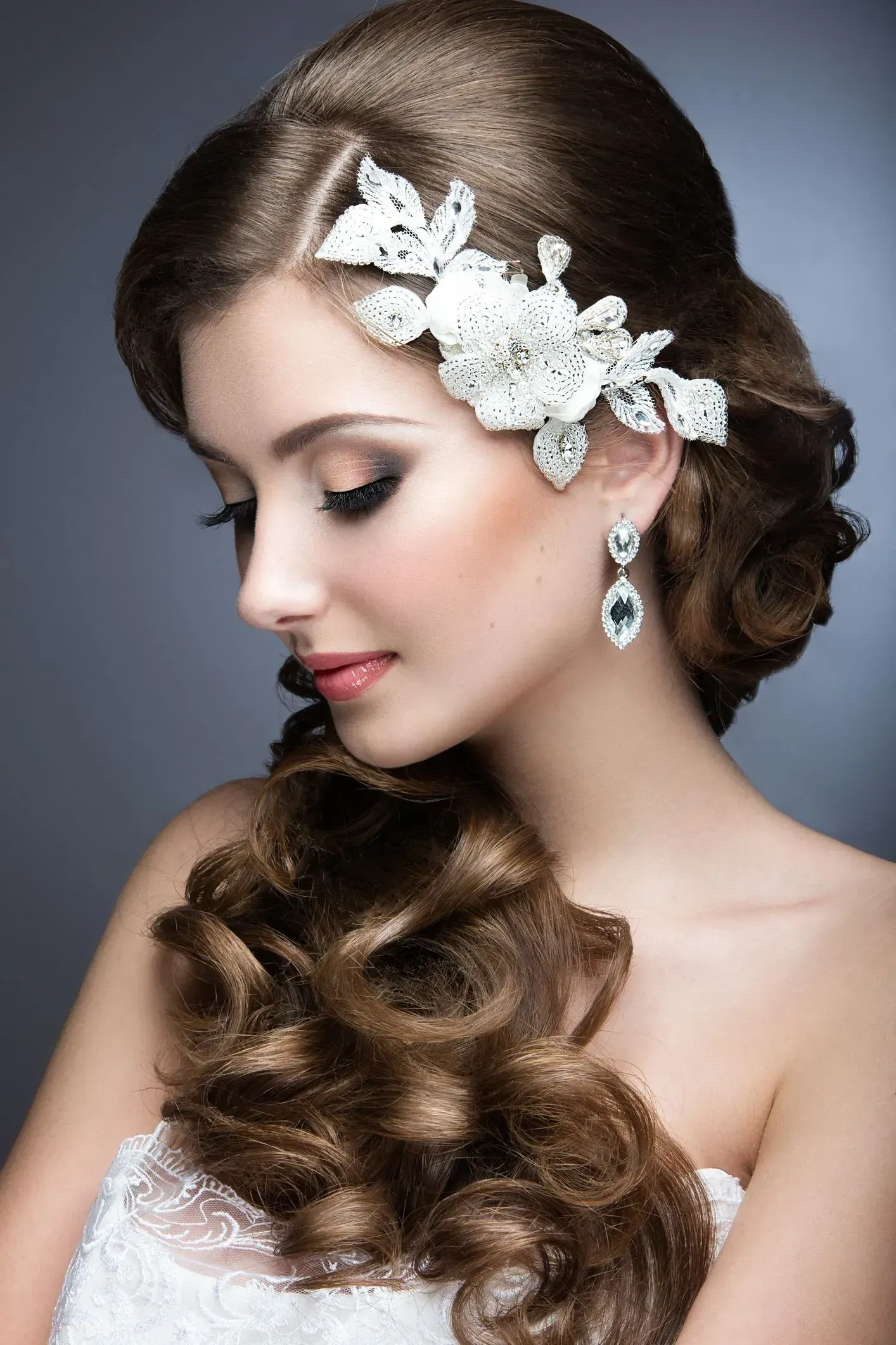 Portrait of a woman with curled brown hair, white floral hairpiece, and drop earrings, looking down gracefully