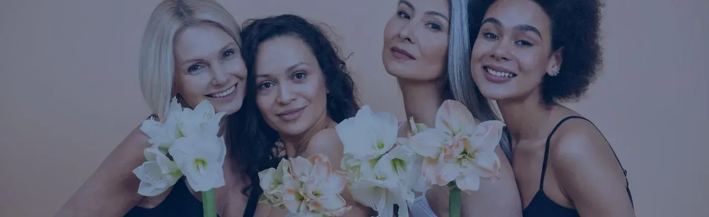 Four smiling friends holding white flowers against a soft pink background
