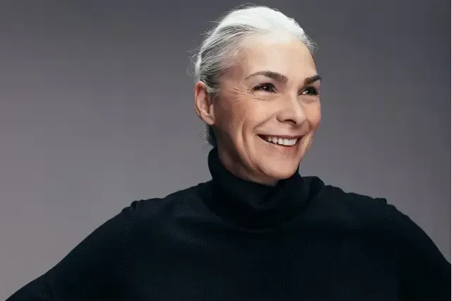 Smiling person in a black turtleneck against a gray background