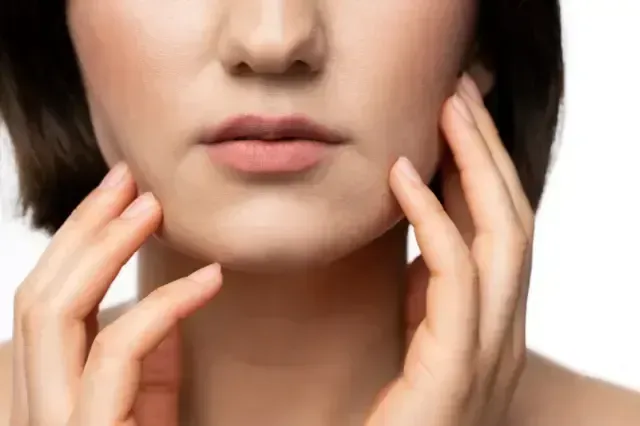 Close-up of a person touching their jaw and cheek, suggesting facial skin care or pain.