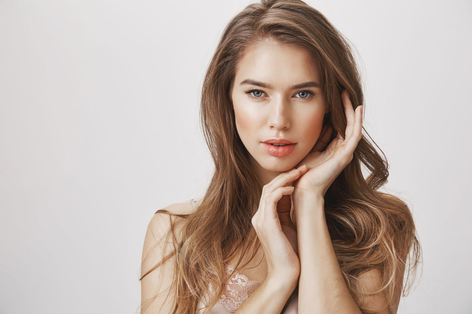 Portrait of a woman with long brown hair, resting her face on her hands against a light background
