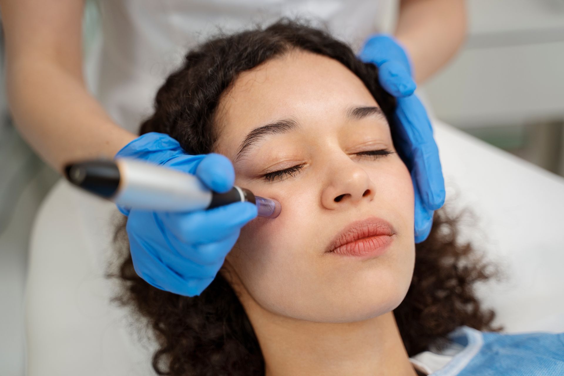 Cosmetologist using a handheld device on a woman’s face during a skincare treatment