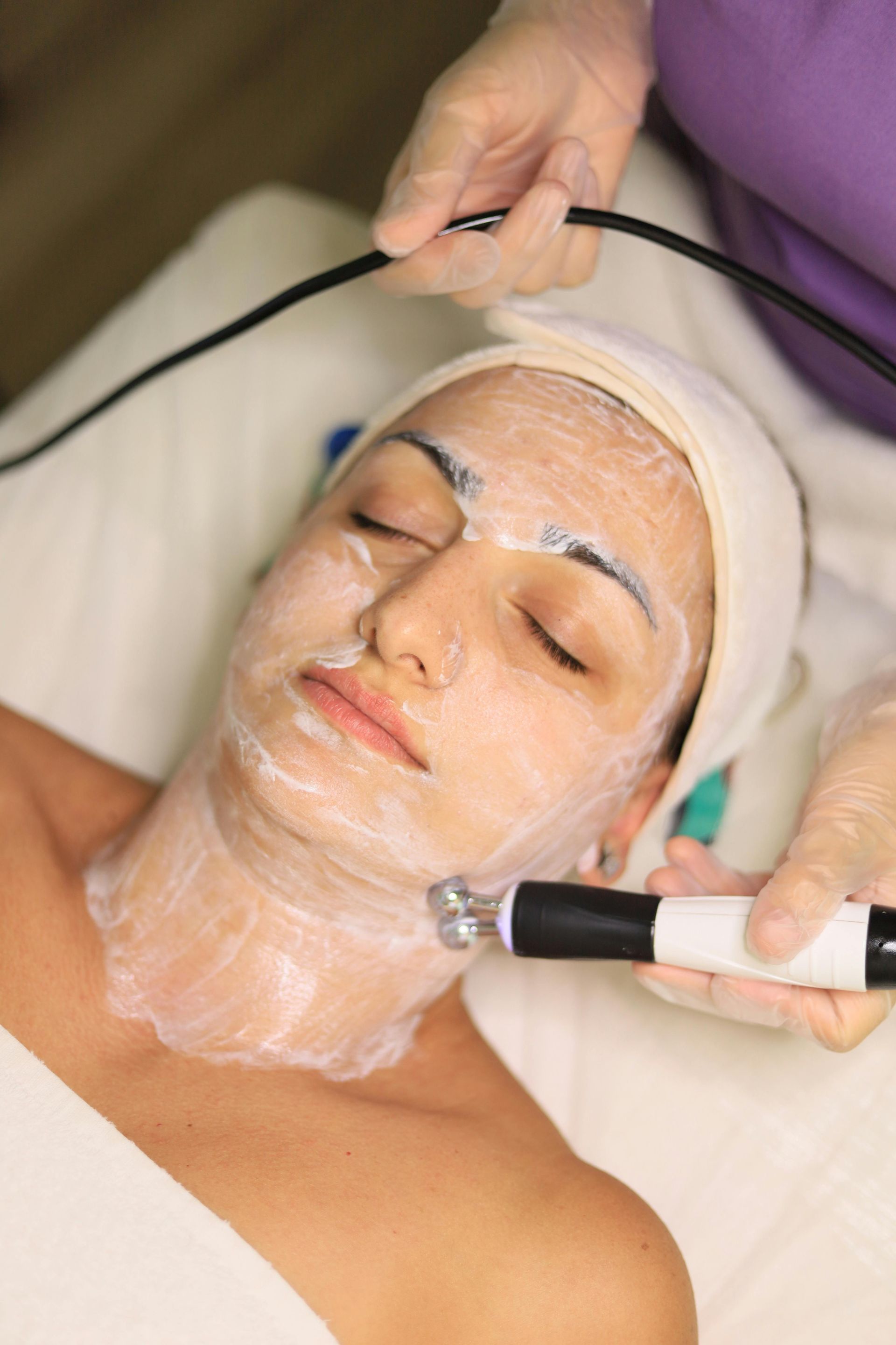 Facial treatment with a gloved hand using a device on a woman’s face in a spa setting