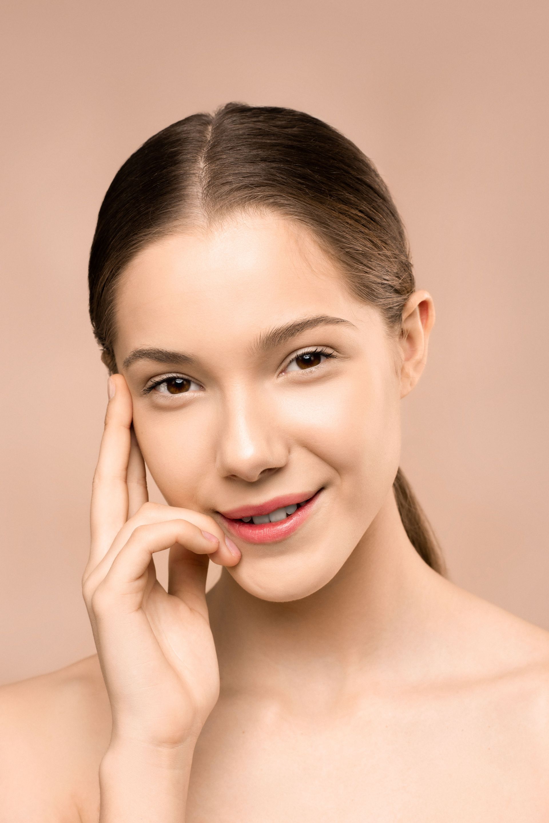 Woman with brown hair posing with hands on her cheeks against a white background