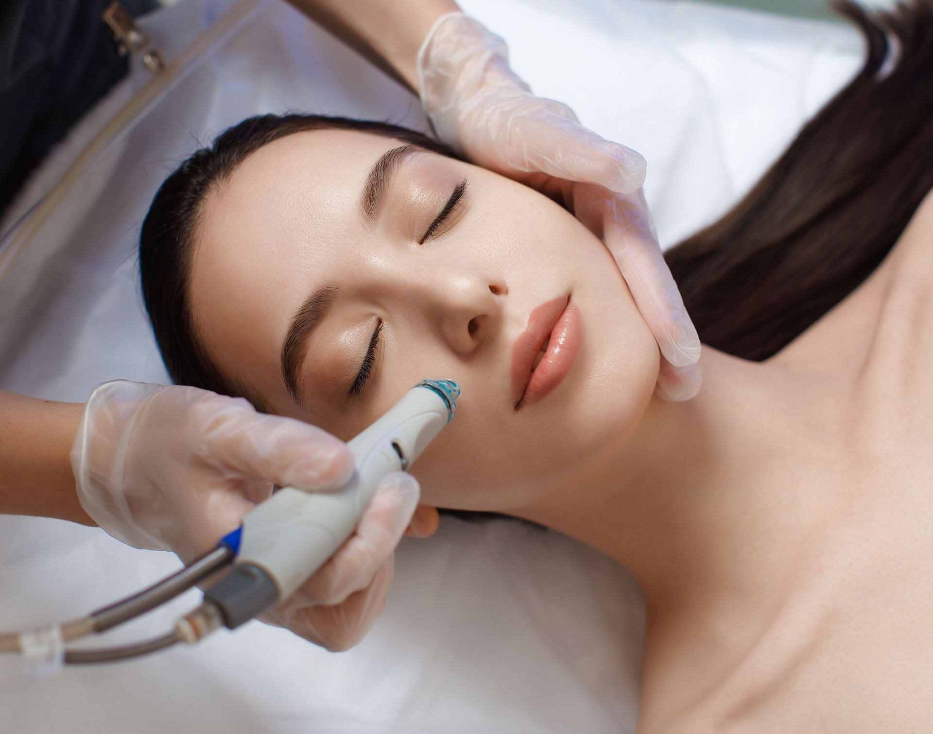 Aesthetic treatment on a woman's face with a handheld device and gloved hands in a clinic setting