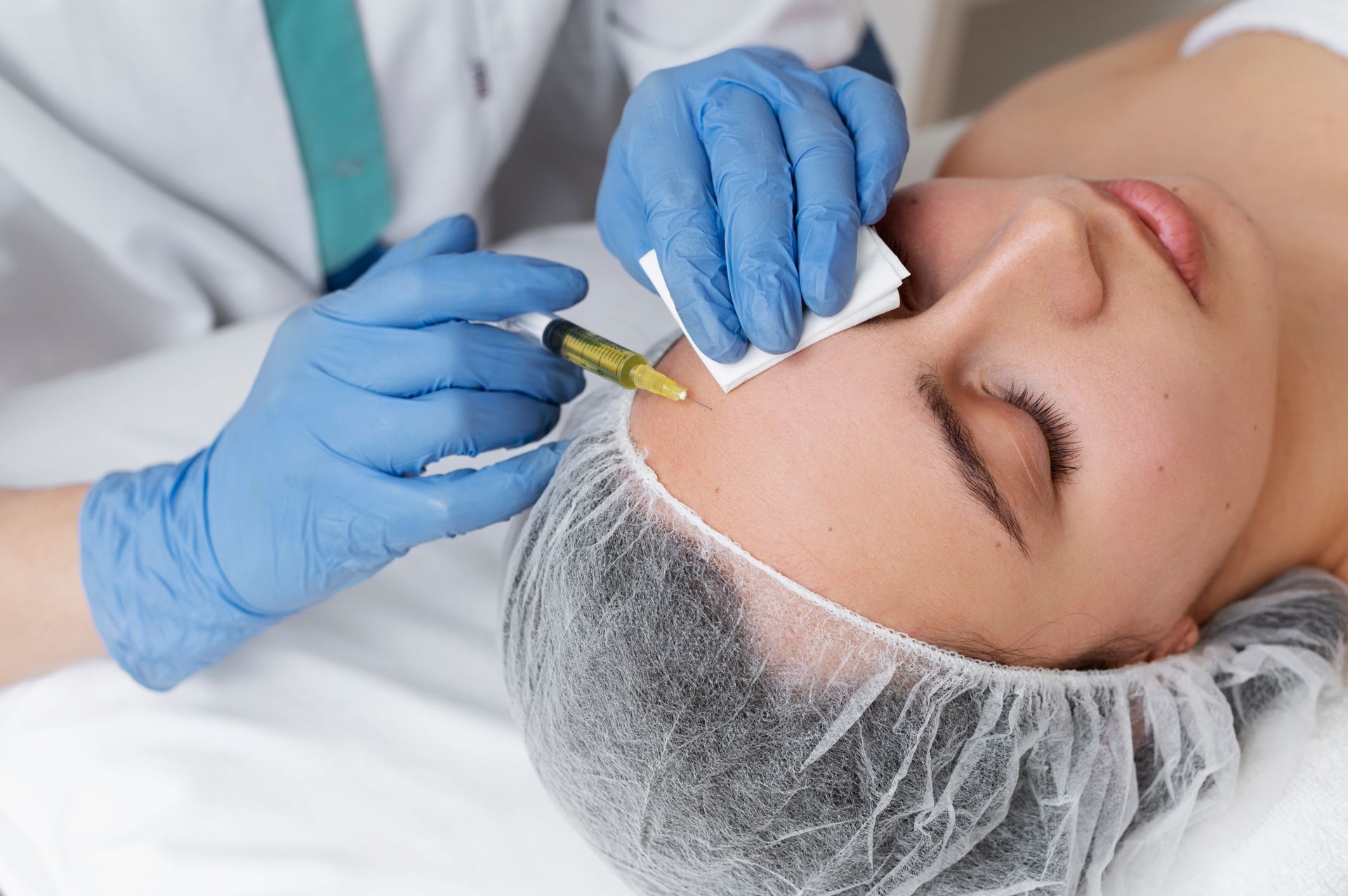 Gloved clinician injects treatment into a patient's forehead in a medical spa setting