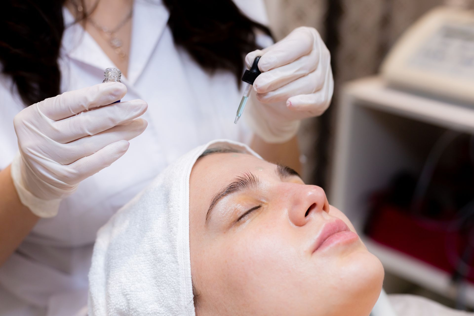 Esthetician applying a facial treatment to a client lying with eyes closed