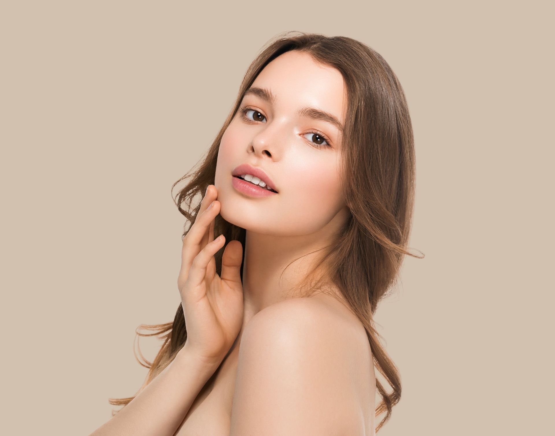 Portrait of a person with wavy brown hair, hand on neck, against a plain beige background