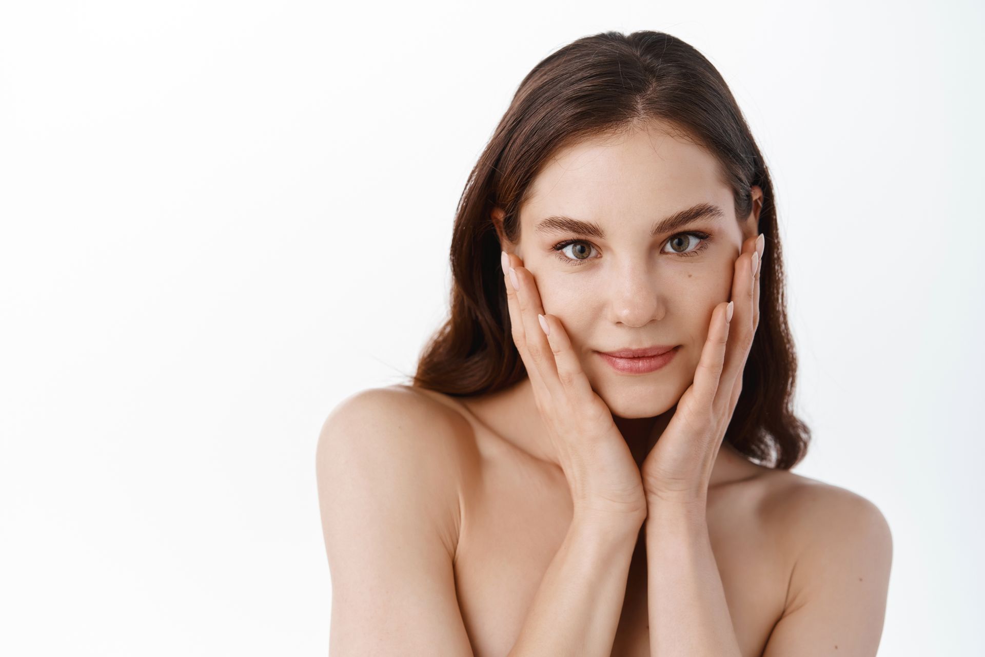 Woman with brown hair posing with hands on her cheeks against a white background
