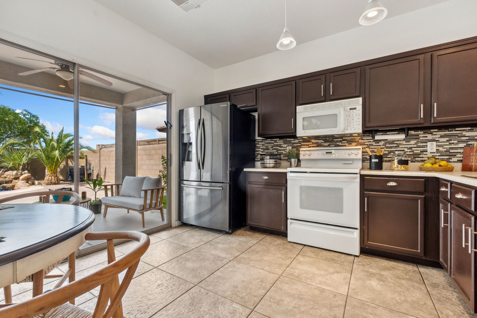Open kitchen with stainless steel appliances, dark cabinets, tiled floor, and sliding glass doors to a patio.