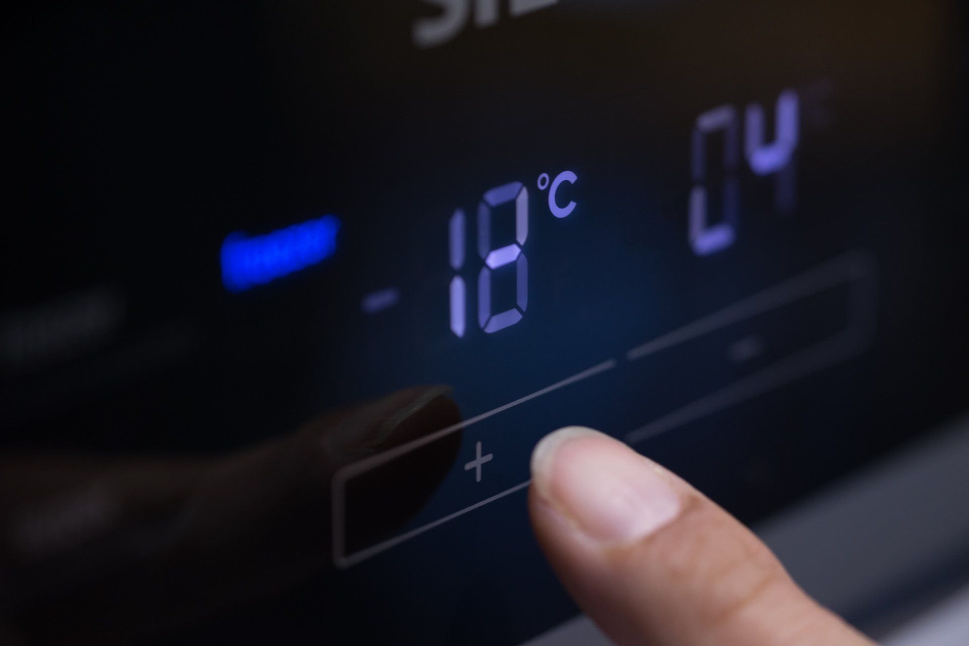 Finger pressing the plus (+) button on a freezer control panel set to -18°C.