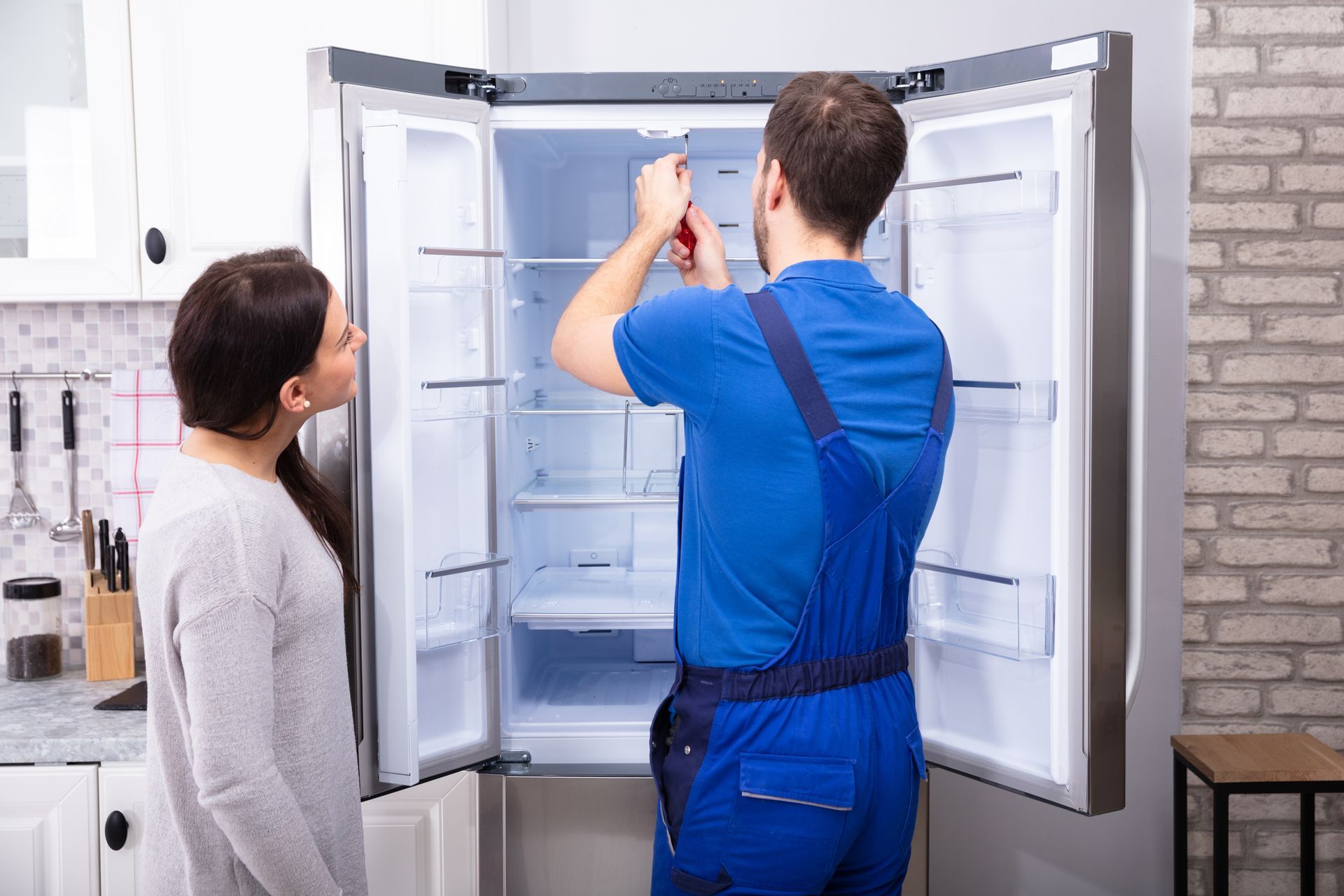 A repairman fixing a refrigerator with a screwdriver. A repairman fixing a refrigerator with a screwdriver.