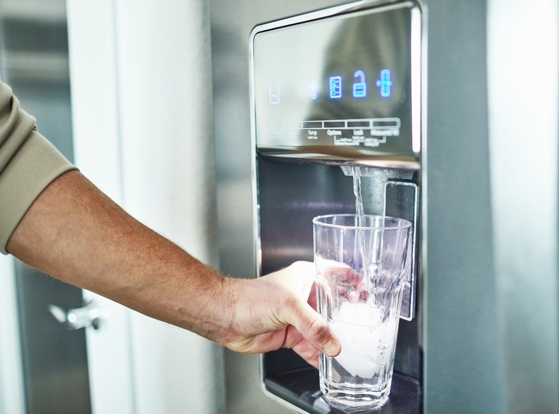 Person filling a clear glass with water from a silver water dispenser, indoors.