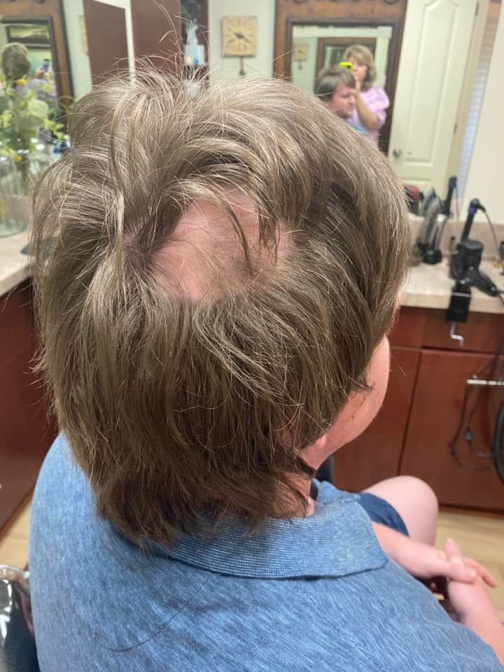 Person with short brown hair and a bald spot in a hair salon.
