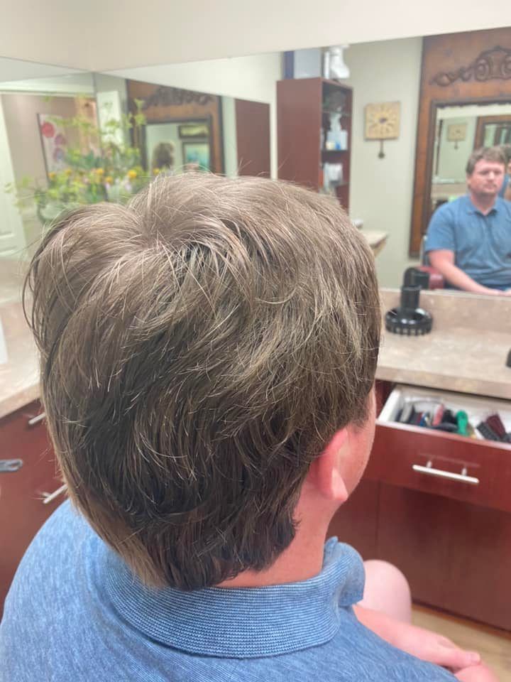 Back of person's head with layered, dark hair in a salon. A man in blue shirt sits across from a mirror.