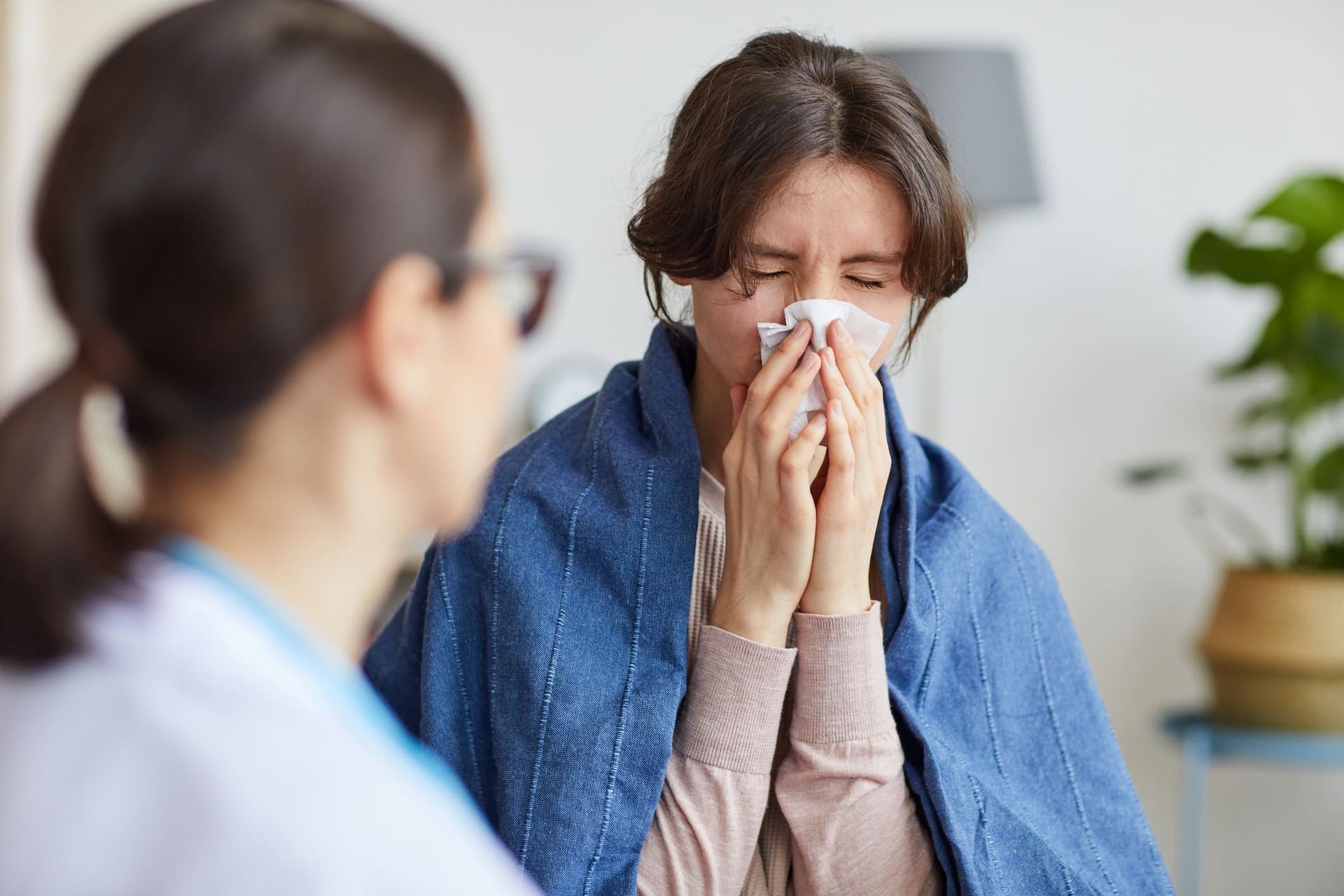 A woman is blowing her nose into a napkin while talking to a doctor.