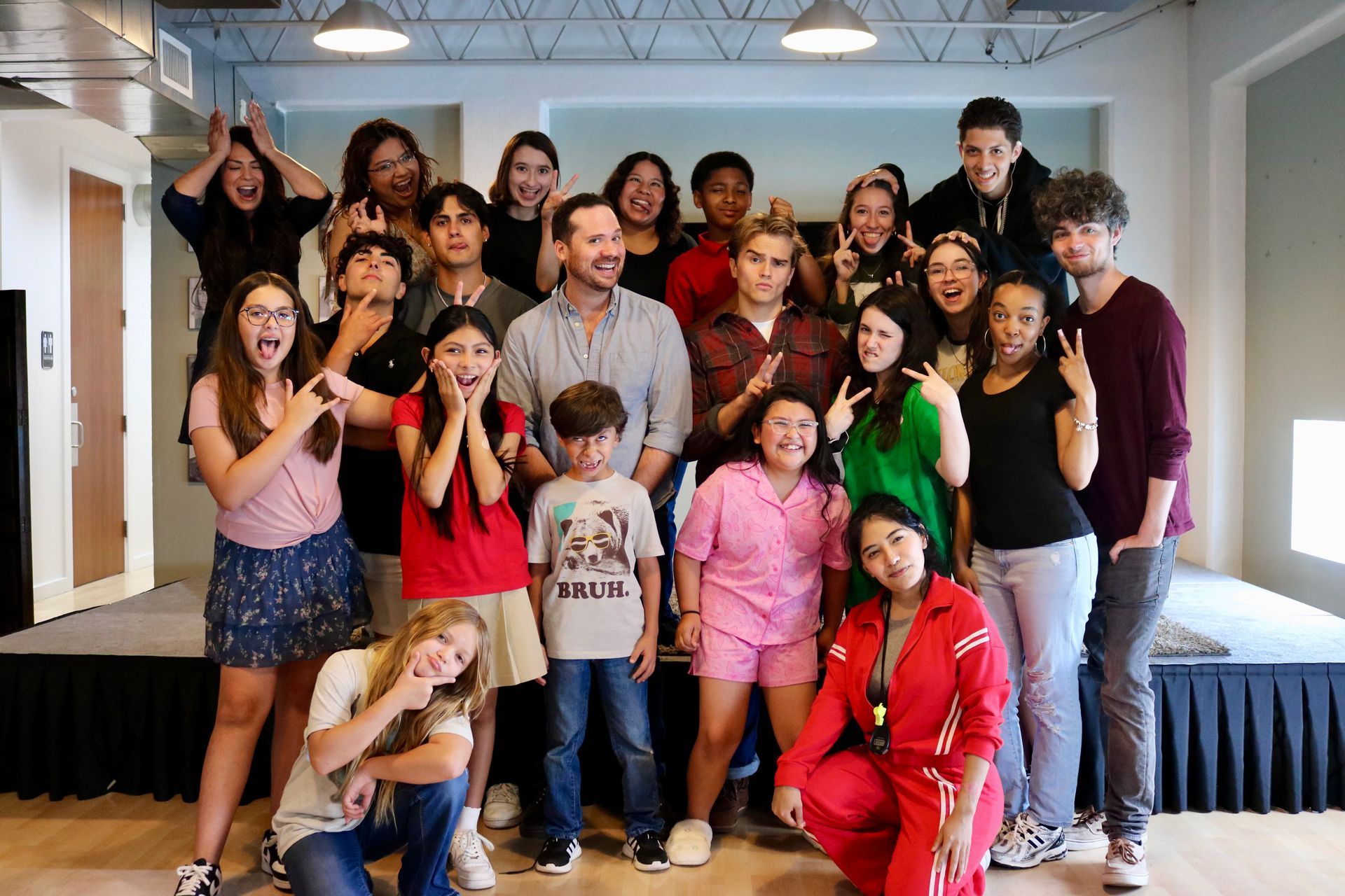 Group of people posing with playful expressions in a room; some making hand gestures.