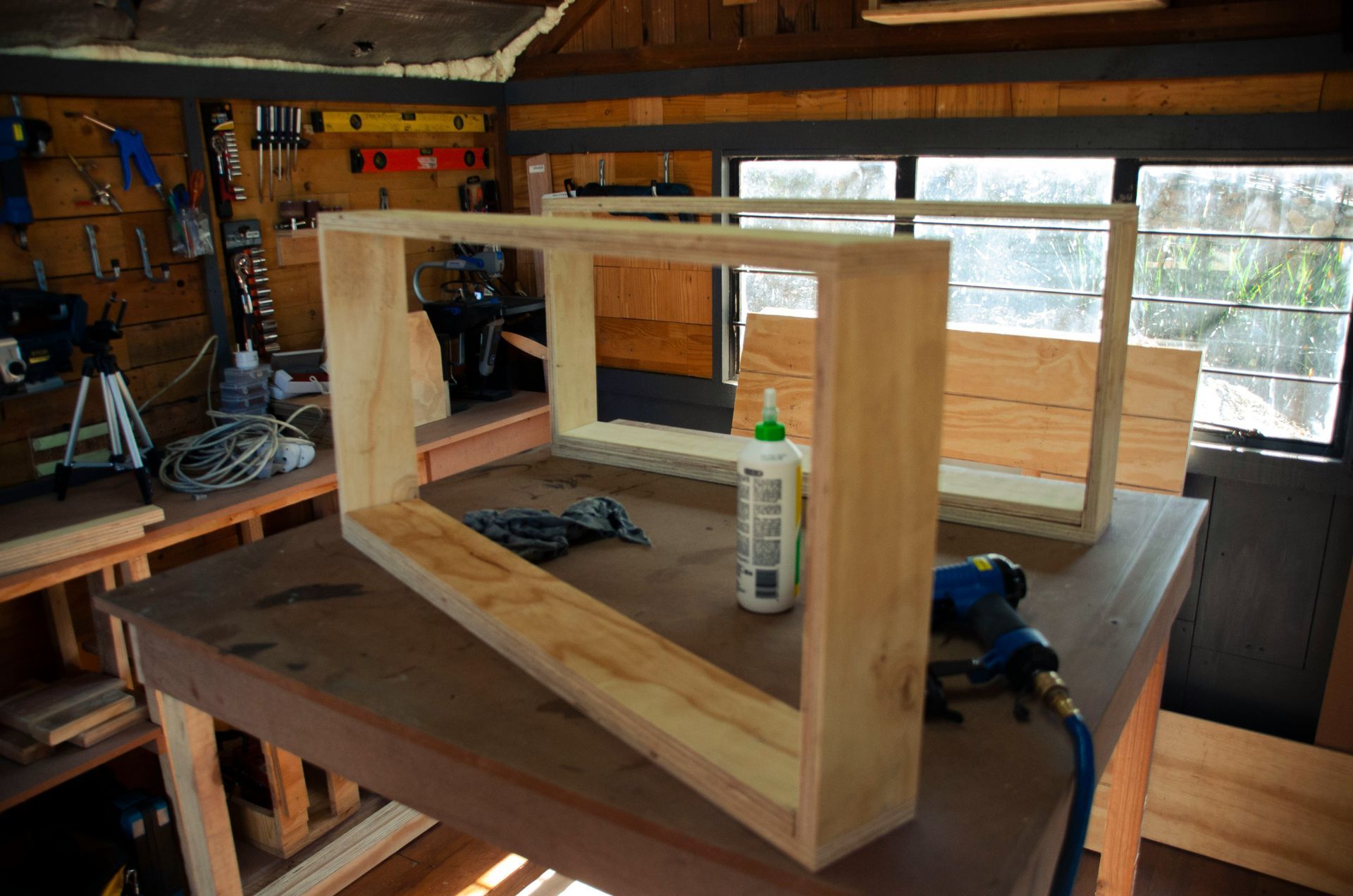 Wooden box frame on a workshop table with tools and glue in a garage-like workspace