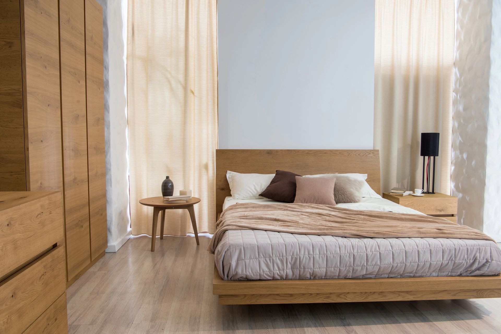 Camera da letto minimalista con letto basso in legno, tende trasparenti e un piccolo comodino.