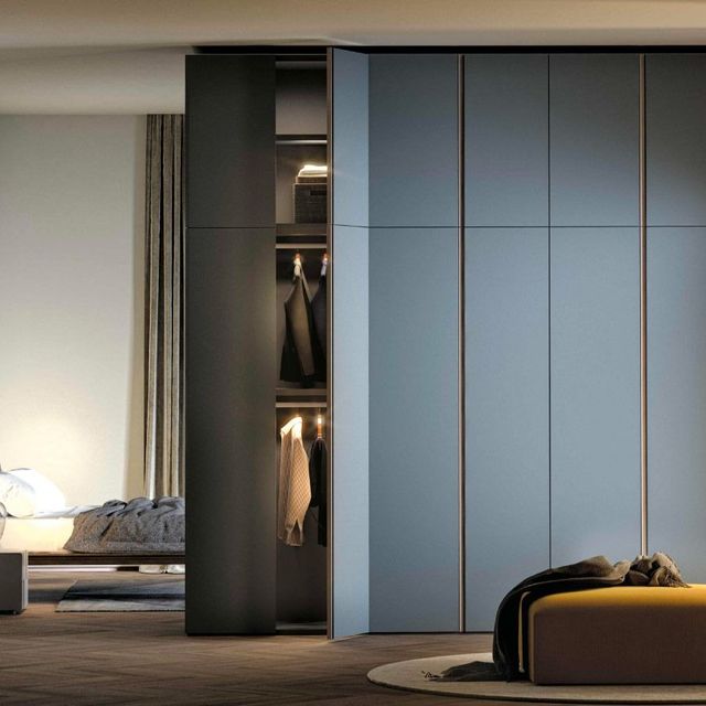 Camera da letto moderna con armadio a vista, ante scorrevoli blu e letto con vestiti piegati.