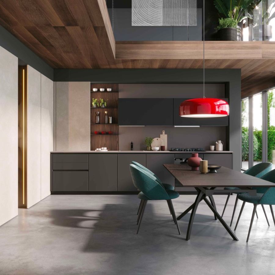 Cucina-sala da pranzo moderna con mobili scuri, sedie verdi, soffitto in legno e lampada a sospensione rossa.