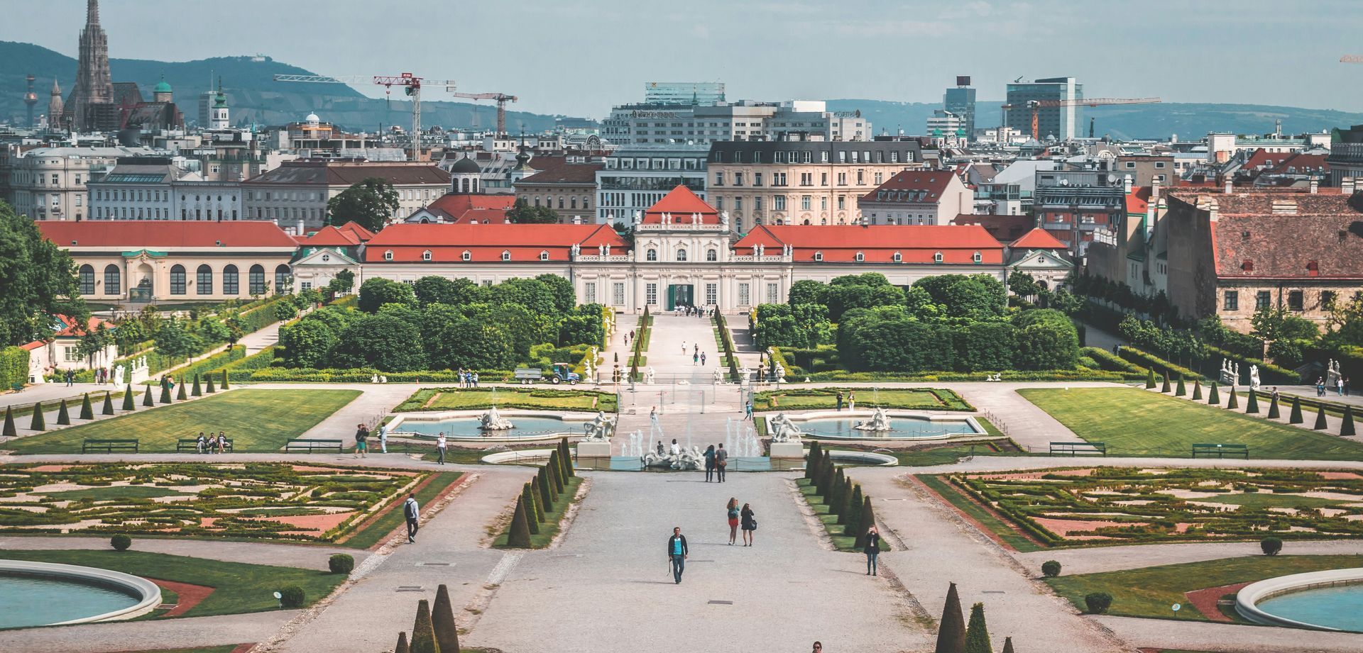 Panoramic view of Belvedere Palace gardens in Vienna with fountains, paths, and city skyline.