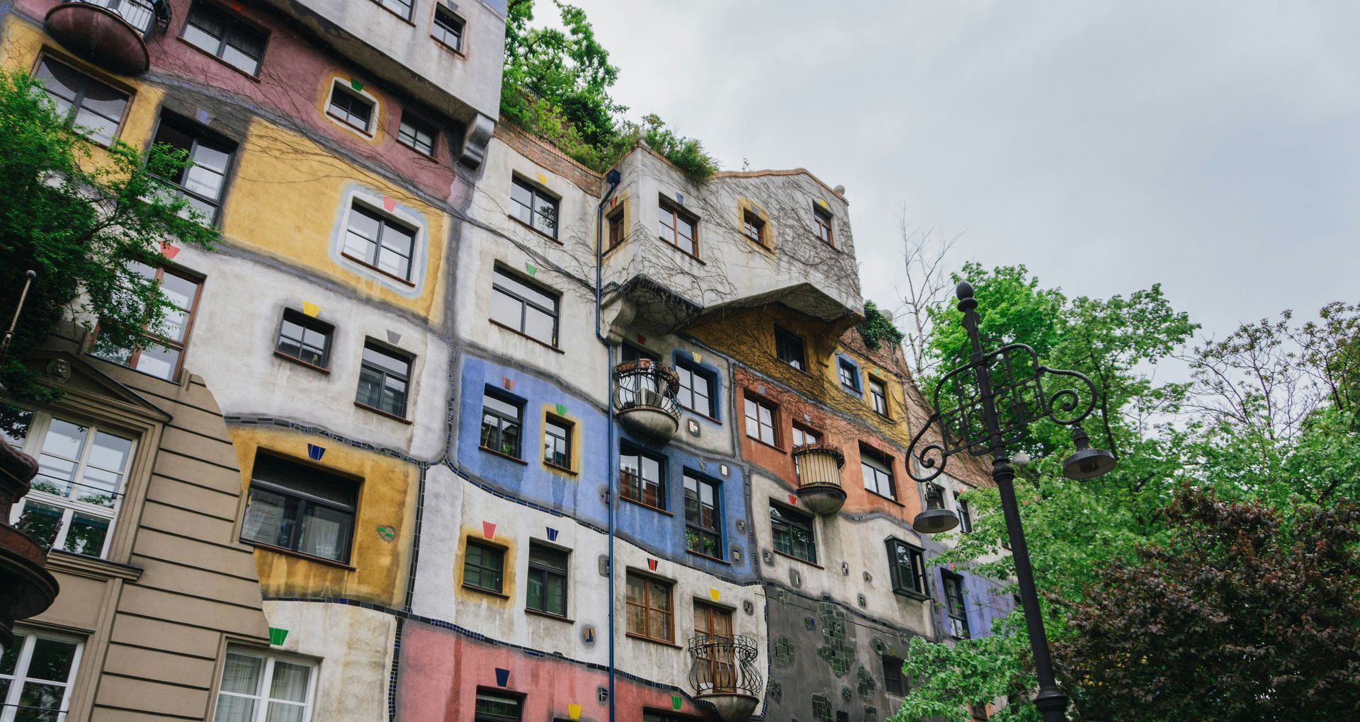 Colorful exterior of Hundertwasserhaus in Vienna, featuring irregular windows, curved lines, and rooftop greenery.