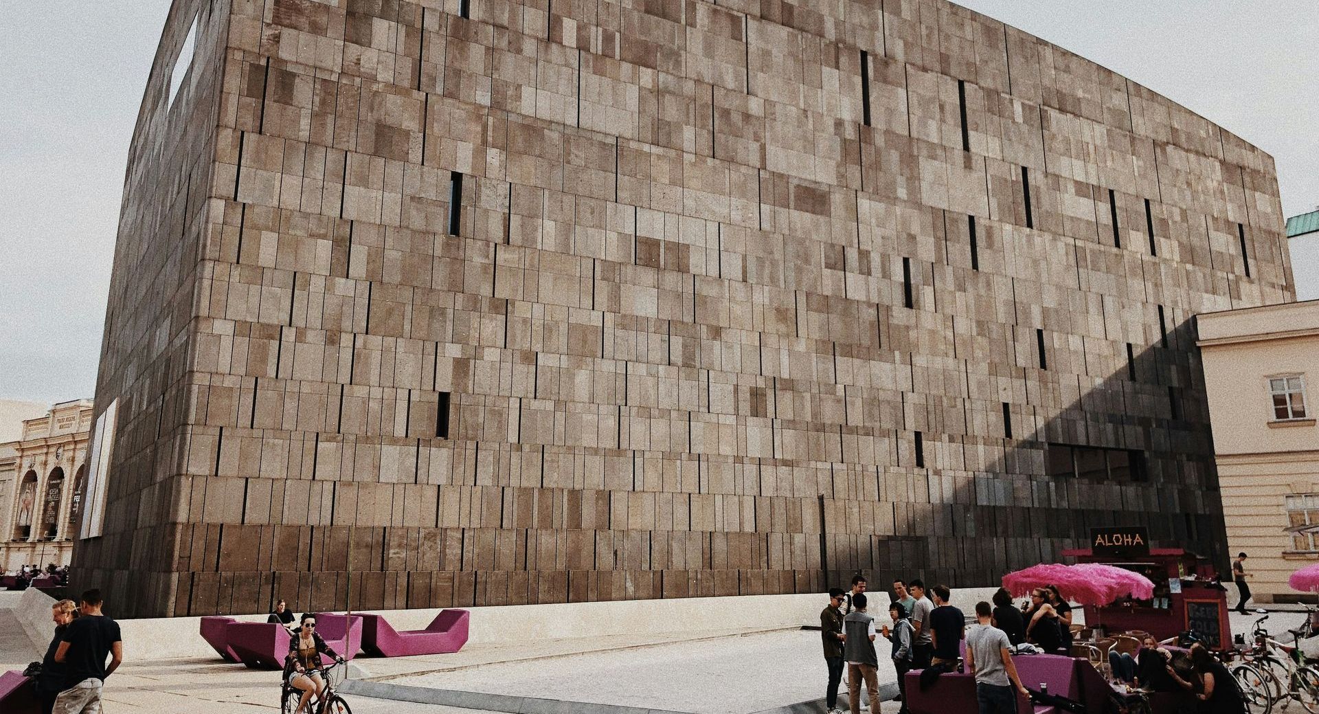 View of the modern facade of the Leopold Museum at MuseumsQuartier in Vienna with people relaxing in the courtyard.