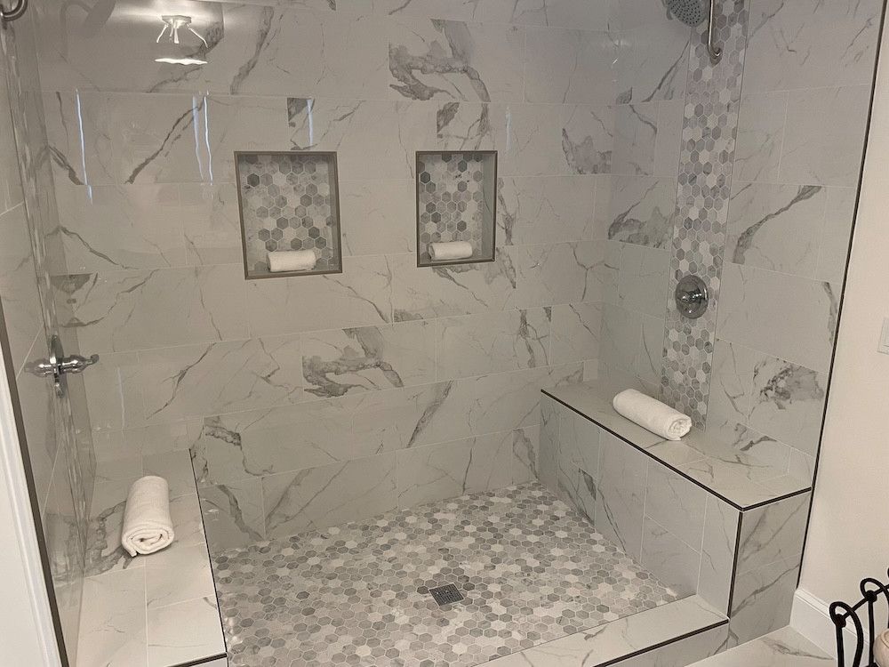 Modern tiled shower with bench, mosaic floor, two recessed shelves, and glass door