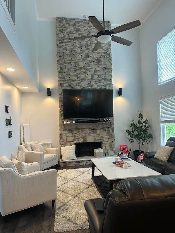 Bright living room with stone fireplace, wall TV, vaulted ceiling, and black leather and white armchairs